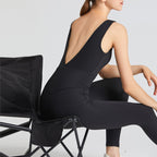 Person wearing a black sleeveless top and leggings sitting on a chair with a plain background