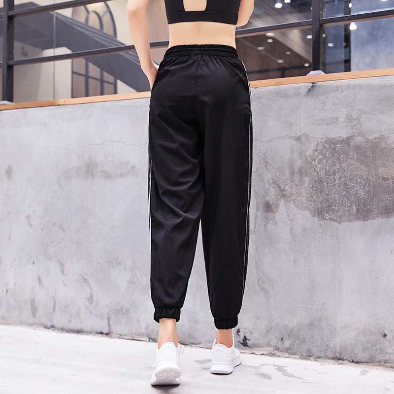 Person wearing black athletic pants with white stripes standing against a concrete wall.