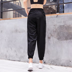 Person wearing black athletic pants with white stripes standing against a concrete wall.