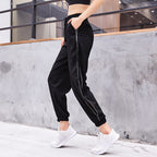 Person wearing black jogger pants with white stripes and white sneakers against a concrete wall.