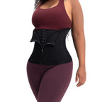 Person wearing a black waist trainer with maroon top and leggings on a white background