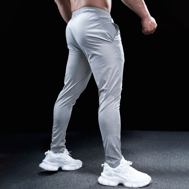 Person wearing light gray athletic pants and white sneakers on a dark background