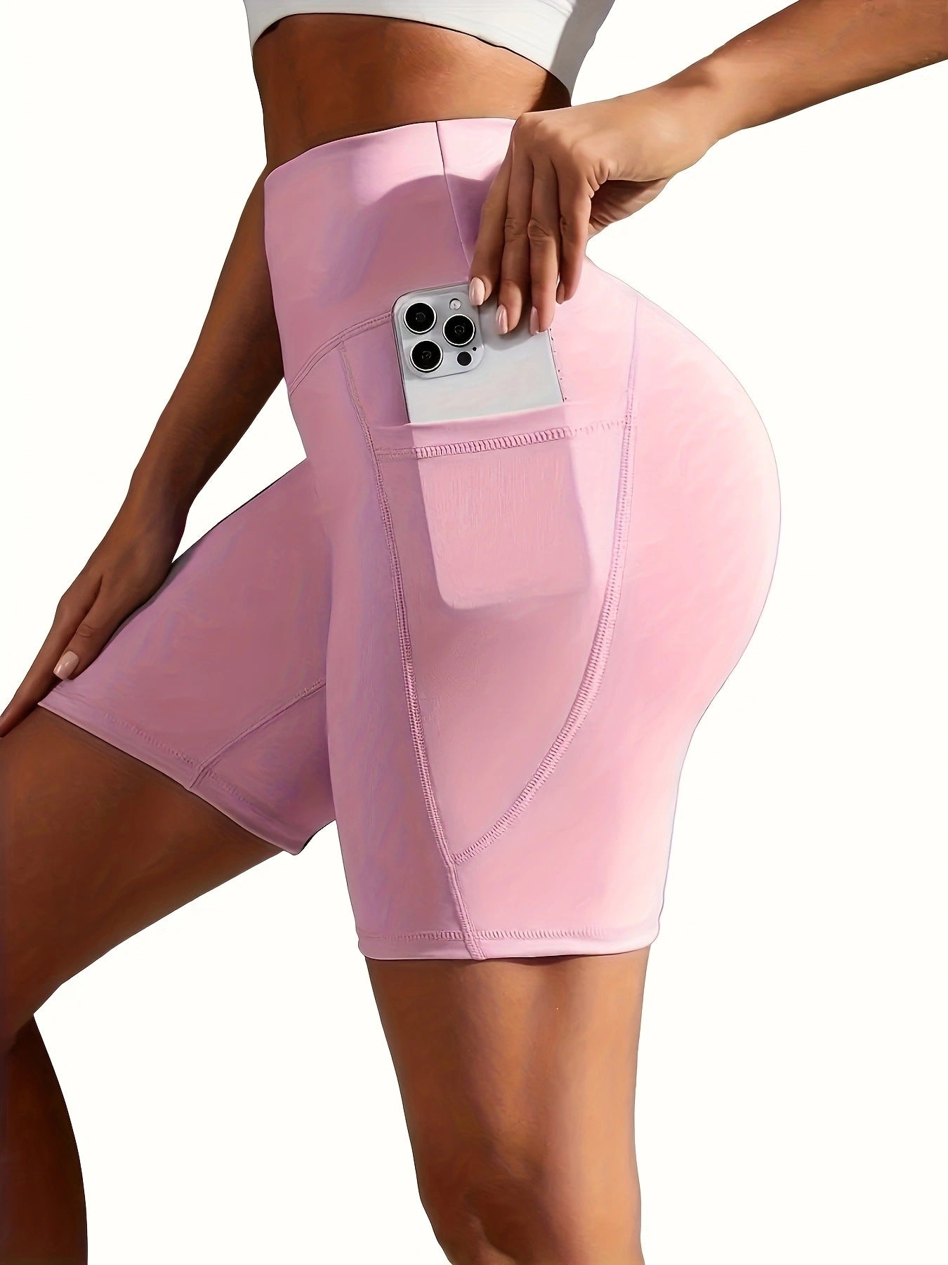 Person wearing pink athletic shorts with a pocket holding a phone on a white background