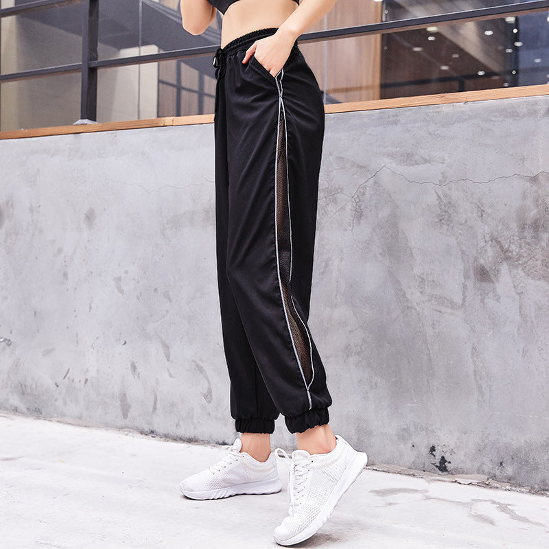 Person wearing black pants with a white stripe and white sneakers against a concrete wall.