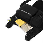 Black sling bag with compartments containing a yellow phone case and a silver wallet on a white background