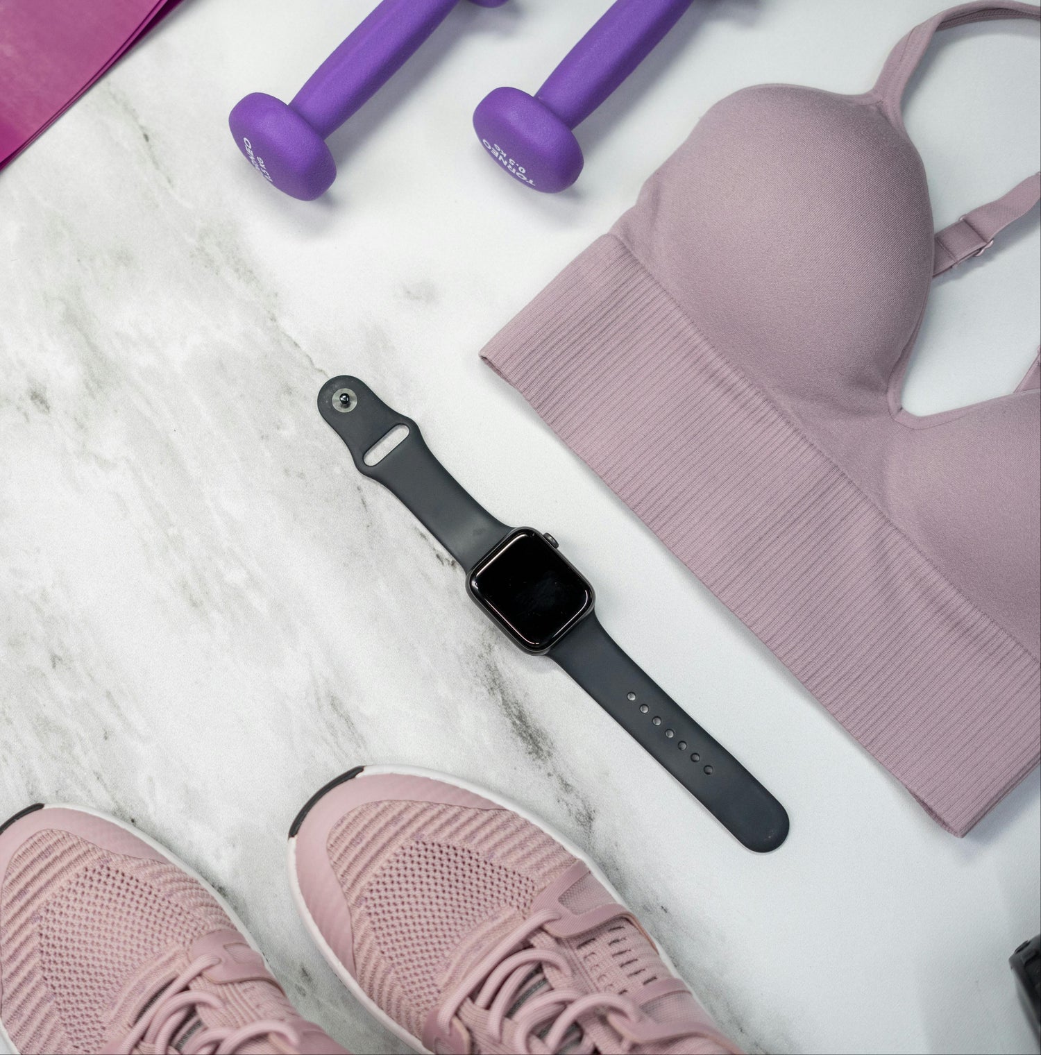 Fitness equipment including a yoga mat, resistance bands, dumbbells, and a smartwatch on a white surface.