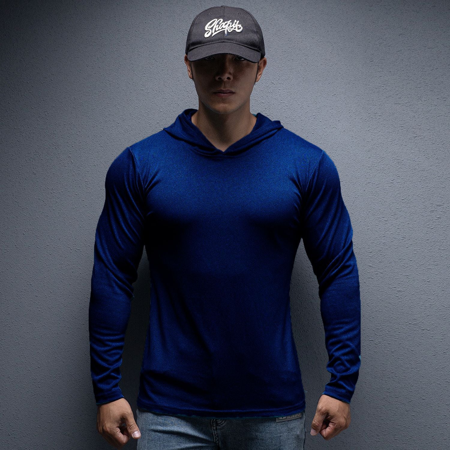 Person wearing a blue long-sleeve shirt and dark cap against a gray background