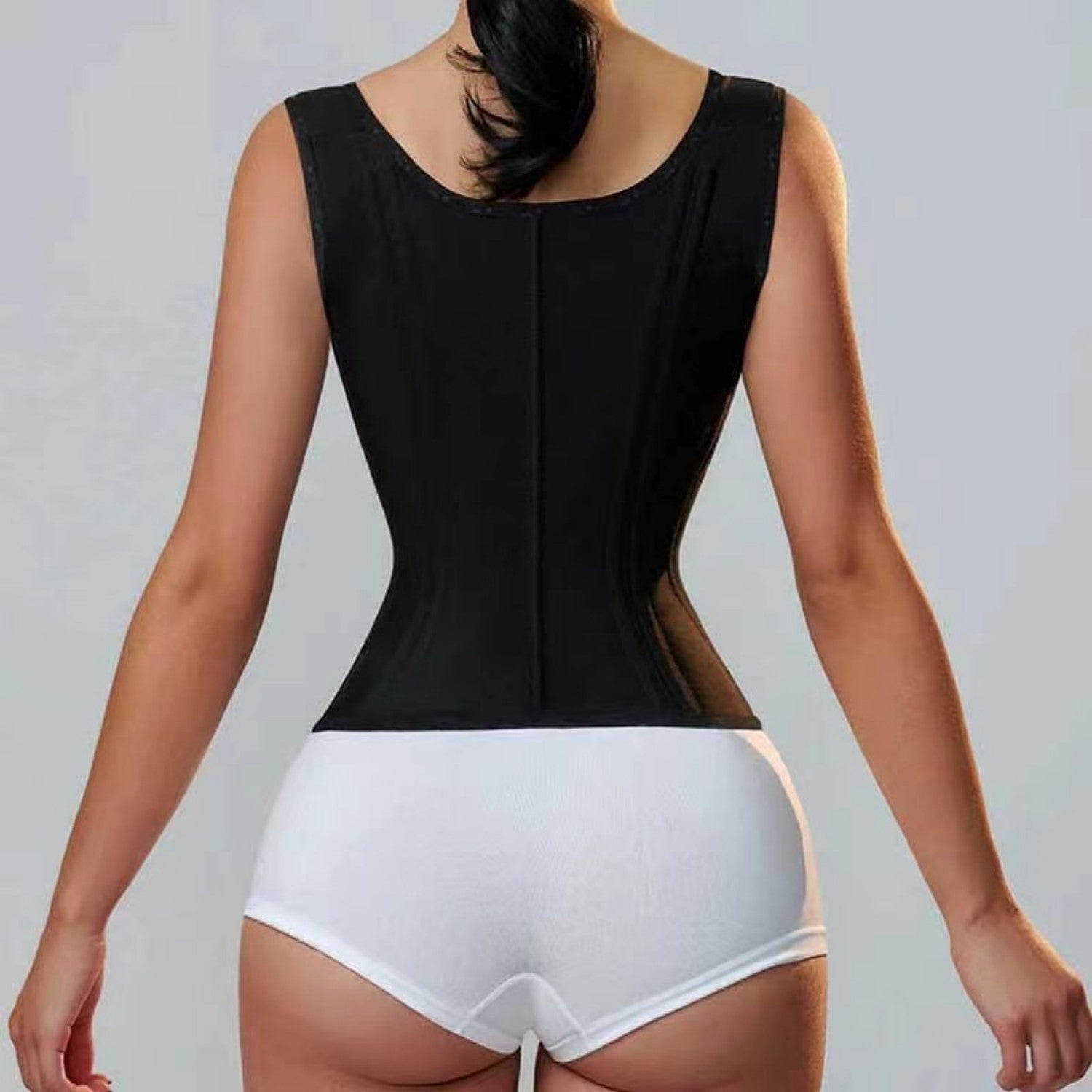 Person wearing a black bodysuit over white underwear on a gray background